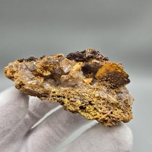 May include: A raw mineral specimen featuring a cluster of translucent, pale crystals embedded within a porous, golden-brown matrix. The rock formation displays jagged edges, earthy textures, and a prominent, flat, amber-coloured crystal shard.