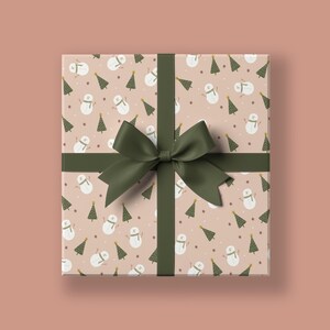 Könnte beinhalten: Eine Geschenkbox, verpackt in rosa Geschenkpapier mit einer grünen Schleife. Das Geschenkpapier hat ein Muster aus kleinen grünen Weihnachtsbäumen und Schneemännern.