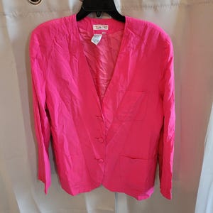 May include: A bright hot pink blazer featuring a V-neckline, long sleeves, and three matching fabric-covered buttons down the front. The jacket includes two lower patch pockets and one chest pocket, with a Talbots label visible at the neck.
