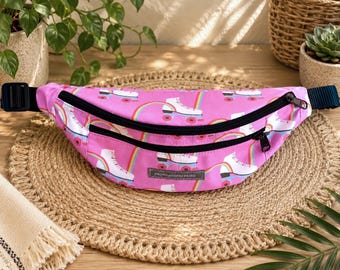 May include: A pink fanny pack featuring a repeating pattern of white roller skates and colorful rainbows. The bag has two black zippered compartments, a black adjustable strap, and a small rectangular grey label with the text Motivation-Holic.