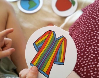 May include: A set of colorful, round, paper cards with various images. The cards feature a rainbow, stars, a globe, an apple, a sheep, and a striped shirt.