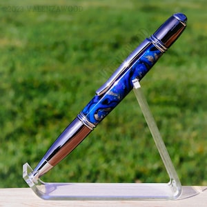 May include: A blue and silver pen with a swirl pattern on the barrel. The pen is on a clear acrylic stand.