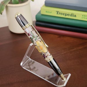 Penna a sfera con meccanismo a torsione, unica nel suo genere, ispirata all'arte popolare scandinava, con elementi floreali dipinti a mano in legno dorato e canna di fucile