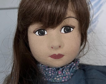May include: A handmade rag doll with long brown hair, brown eyes, and a blue dress with a floral print collar.