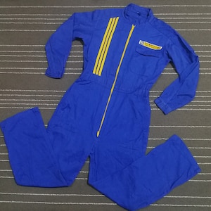 Pode incluir: Macacão de trabalho azul com listras amarelas e um logotipo da Caterpillar no peito.