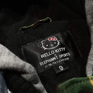 K&ouml;nnte beinhalten: Schwarz-gr&uuml;ner Kapuzenpullover mit einem Hello Kitty x Elephant Sports-Etikett. Das Etikett zeigt eine Hello Kitty-Karikatur mit einer roten Schleife und den Text "Hello Kitty x Elephant Sports &copy;'16 '11 Sanrio 9".