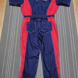 May include: A blue and red Daihatsu racing jumpsuit. The jumpsuit features a blue torso and legs with red side panels and white stitching. The word "DAIHATSU" is printed in white across the upper back.