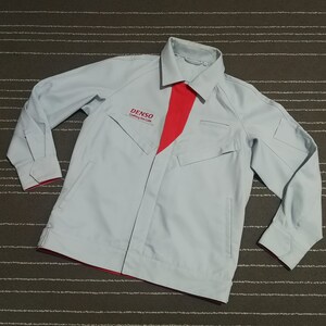 May include: A pale blue work jacket with a red panel on the front and collar. The jacket features long sleeves, two front pockets, and the "DENSO" logo. It is made from a robust material, suitable for work. The jacket's design is practical and functional.