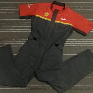 Pode incluir: Um macacão de mecânico preto e vermelho com o logotipo da Shell Helix no peito. O macacão tem mangas compridas e um fecho de correr.