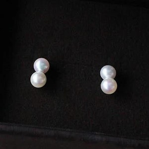 May include: A pair of pearl earrings in a black velvet jewelry box. The earrings are made of two small pearls each.