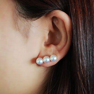 May include: A close-up of a woman's ear wearing a pearl earring with three pearls in a row. The earring is made of 18k or 14k white gold and the pearls are 7.5mm in diameter.