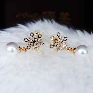 May include: A pair of gold snowflake earrings with a dangling pearl on each earring.
