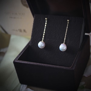 May include: A pair of pearl drop earrings with a gold chain. The earrings are in a black velvet box.