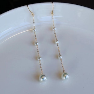 May include: A pair of long gold earrings with white pearls hanging from a delicate chain.