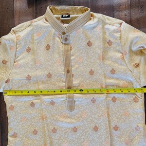 Pu&ograve; includere: Camicia kurta color crema con motivo floreale e colletto alla coreana. La camicia ha un'abbottonatura frontale e viene misurata con un metro a nastro giallo. La lunghezza della camicia &egrave; di circa 28 cm.