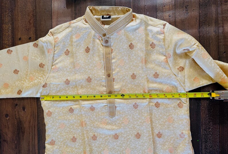 Pu&ograve; includere: Camicia kurta color crema con motivo floreale e colletto alla coreana. La camicia ha un'abbottonatura frontale e viene misurata con un metro a nastro giallo. La lunghezza della camicia &egrave; di circa 28 cm.