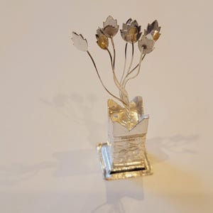May include: A silver decorative flower arrangement with a silver base. The flowers are made of silver and have a slightly gold tone.