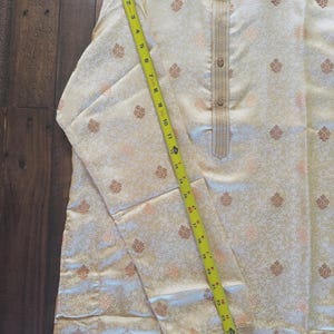 Pu&ograve; includere: Kurta color crema con motivo floreale e colletto alla coreana. L'indumento a maniche lunghe ha una chiusura frontale con bottoni ed &egrave; misurato con un metro a nastro giallo. La kurta &egrave; lunga circa 63,5 cm.