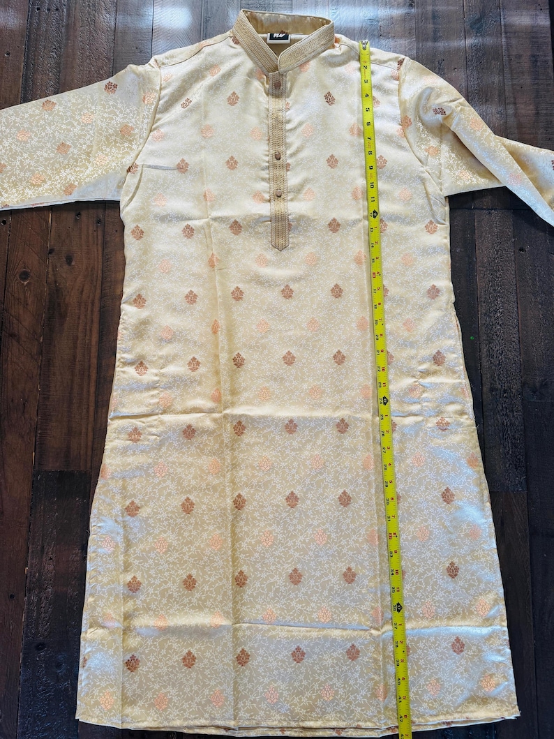 Pu&ograve; includere: Kurta color crema con colletto alla coreana e maniche lunghe. Il tessuto presenta un motivo ripetuto di piccoli motivi floreali stilizzati nei toni del pesca e dell'oro. La kurta &egrave; lunga circa 102 cm.