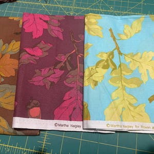 May include: Three fabric panels featuring leaf designs in brown, magenta, and light blue. The brown fabric has yellow and orange leaves, the magenta fabric has pink leaves, and the blue fabric has yellow leaves. Each panel has a white border with text.