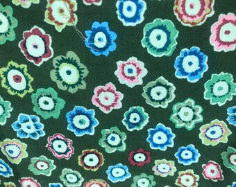 May include: A green fabric with a repeating pattern of colorful flowers. The flowers have a white center and are surrounded by different colored rings.