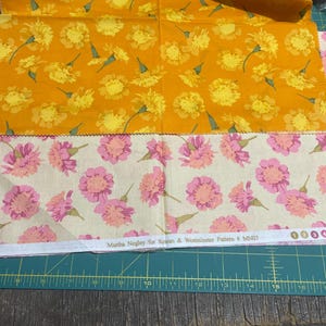 May include: Three fabric swatches. The top swatch is a bright orange with yellow floral patterns. The middle swatch is a cream colour with pink floral patterns. The bottom swatch is a cream colour with pink floral patterns. The text "Martha Negley for Rowan & Westminster Pattern # MN07" is visible.