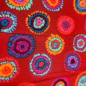 May include: Red fabric with a repeating pattern of colourful circular designs. The circles have a tie-dye effect with shades of pink, orange, blue, green, and purple.