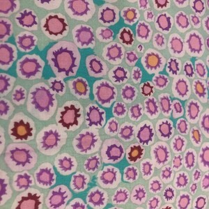 以下が含まれることがあります： ターコイズ色の生地に、ピンク、パープル、オレンジの花が繰り返しパターンで描かれています。花は白い輪郭で、生地全体に散りばめられています。