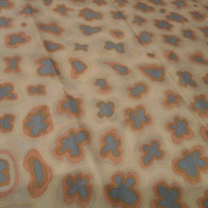 May include: A beige fabric with a repeating pattern of blue and orange abstract shapes. The shapes are outlined in orange and have a light blue centre.