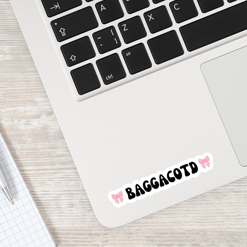Op de afbeelding: Een laptop met een sticker waarop "Baggacotd" staat, met twee roze strikken aan weerszijden van de tekst.