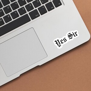 May include: A silver laptop computer with a white sticker that says "Yes Sir" in black old English font.