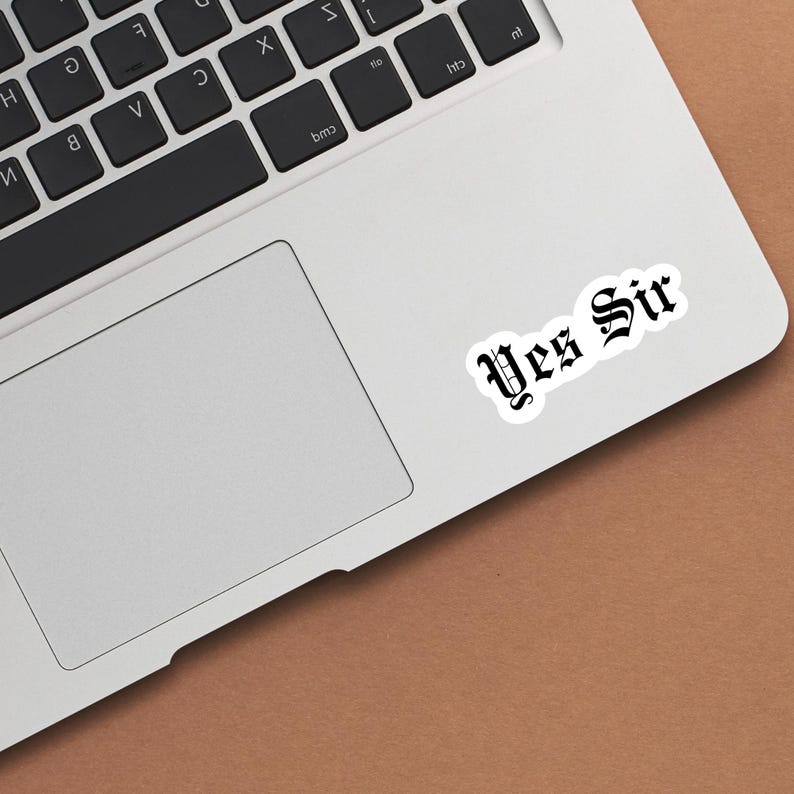 May include: A silver laptop computer with a white sticker that says "Yes Sir" in black old English font.