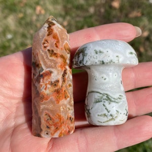May include: Two polished agate crystal carvings: a tall, pointed tower with brown, orange, and white patterns, and a mushroom-shaped carving with white and green patterns.