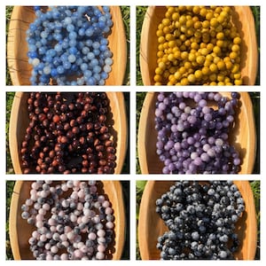 May include: Assortment of six different types of gemstone beads in wooden bowls. The beads are blue, yellow, red, purple, pink, and black.