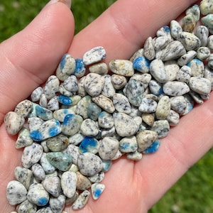 Könnte beinhalten: Ein Haufen kleiner, getrommelter blauer Kyanit-Steine mit weißen und grauen Markierungen. Die Steine sind glatt und haben ein natürliches, poliertes Aussehen.