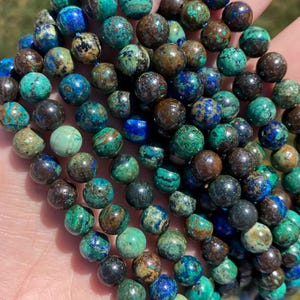 Puede incluir: Una hebra de cuentas redondas de piedras preciosas verdes, marrones y azules. Las cuentas tienen un diámetro aproximado de 8 mm y presentan un aspecto moteado natural.