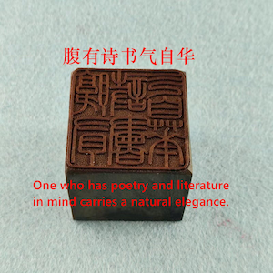Puede incluir: Un sello de madera marrón con caracteres chinos y el texto en inglés: "One who has poetry and literature in mind carries a natural elegance." El sello tiene una base rectangular.
