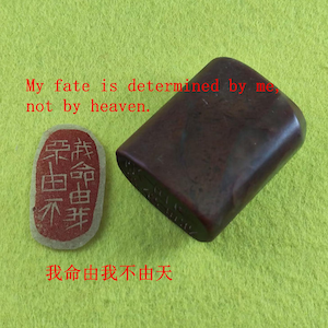 Puede incluir: Un sello rectangular marrón oscuro y un sello rojo y blanco con caracteres chinos. El sello dice: "Mi destino está determinado por mí, no por el cielo". El sello tiene caracteres tallados en su lado.