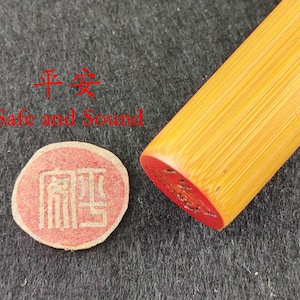 Puede incluir: Primer plano de un sello de bambú con tinta roja y las palabras "Safe and Sound" en inglés y caracteres chinos. El sello es redondo y el mango es cilíndrico.