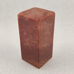 May include: A square-shaped stone seal with a rough texture, in shades of red and brown.