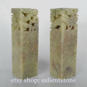 Könnte beinhalten: Zwei rechteckige Siegel aus grünem Stein mit aufwendig geschnitzten Drachenmotiven. Die Siegel sind etwa 15 cm hoch und haben eine hellgrüne Farbe mit braunen und grauen Streifen.