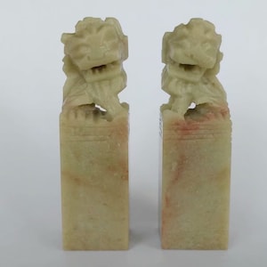 May include: Pair of green stone Chinese lion sculptures, each with a detailed carving of a lion's head and body, mounted on a rectangular base.