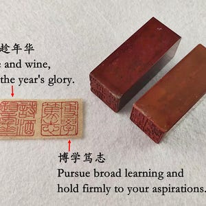 Puede incluir: Dos sellos rectangulares de piedra marrón rojizo con diseños tallados, junto a un pequeño papel rectangular con caracteres chinos rojos. El texto en inglés y chino dice: "Verse and wine, seize the year's glory." y "Pursue broad learning and hold firmly to your aspirations."