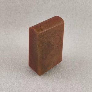 May include: A rectangular bar of brown soap with a slightly rounded top. The soap has a mottled appearance, with shades of brown, orange, and red.
