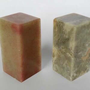 May include: Two rectangular stone blocks, one is a light green with white and brown marbling, the other is a light green with a reddish brown hue.