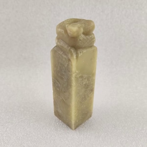 Könnte beinhalten: Eine kleine, rechteckige Steinskulptur in hellgrüner Farbe mit einem detaillierten Design auf der Oberseite. Die Skulptur ist wahrscheinlich ein traditionelles chinesisches Siegel.