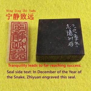 Puede incluir: Un sello rectangular negro con caracteres chinos blancos y una impresión de sello rojo sobre un papel rectangular. El texto dice "Ning Jing Zhi Yuan" y "La tranquilidad conduce al éxito."