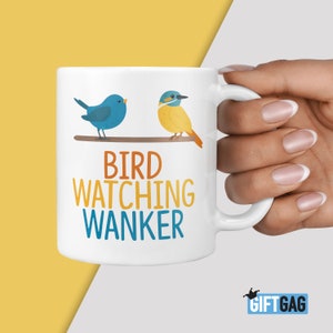 May include: White ceramic mug with the text "BIRD WATCHING WANKER" in orange and blue. The mug features illustrations of two birds perched on a branch. A blue bird is on the left, and a yellow and orange bird is on the right.