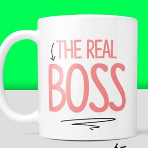 Puede incluir: Taza de cer&aacute;mica blanca con una flecha negra apuntando hacia abajo al texto "THE REAL BOSS" en letras rosas.