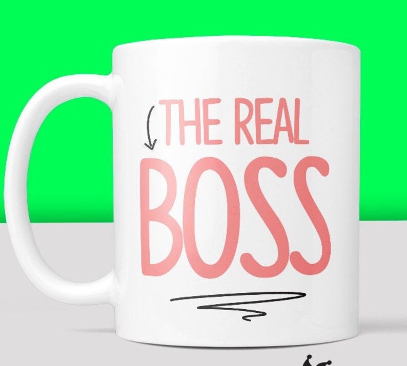 Puede incluir: Taza de cer&aacute;mica blanca con una flecha negra apuntando hacia abajo al texto "THE REAL BOSS" en letras rosas.